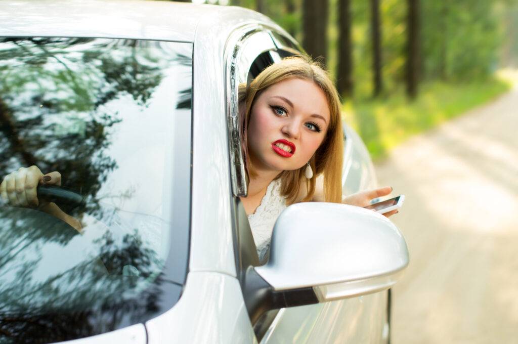 Una bella ragazza guarda fuori dal finestrino dell'auto e impreca con forza, creando una situazione di negatività