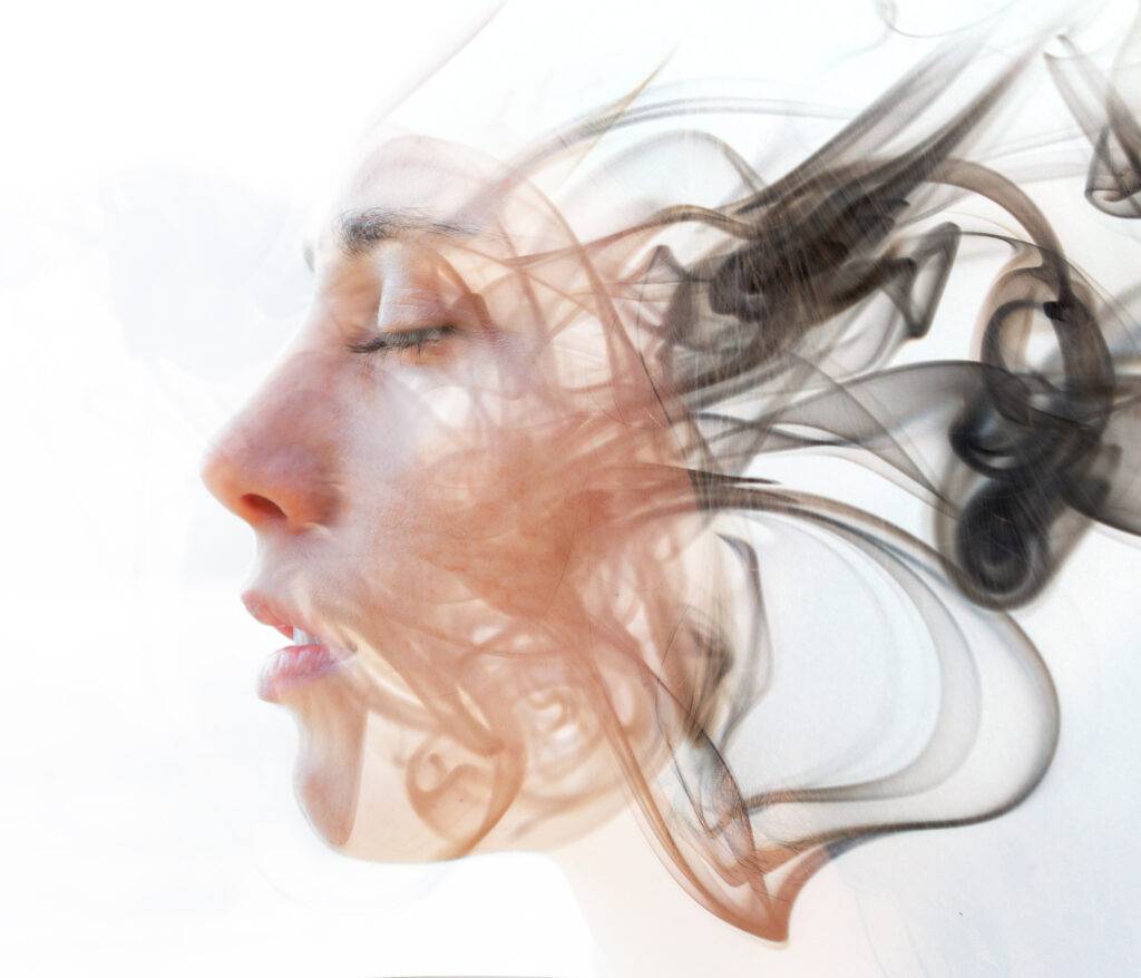 Ritratto in doppia esposizione di una giovane donna dalla pelle chiara e una texture fumosa che si dissolve nei suoi tratti del viso - Comprendi le Tue Forze Naturali
