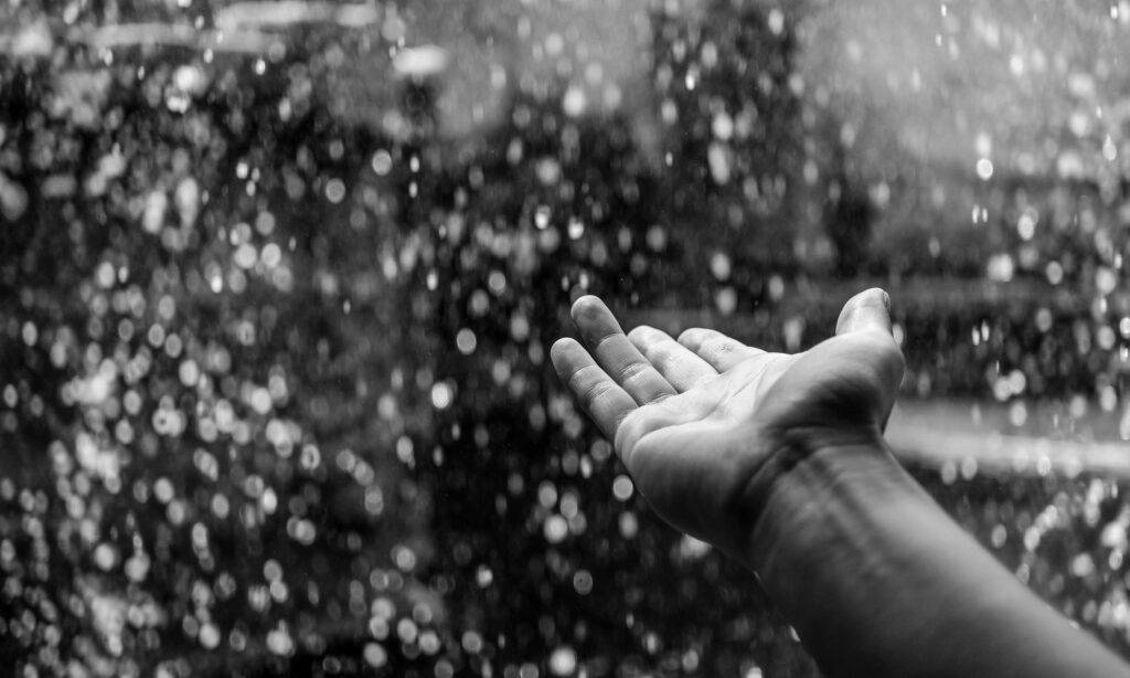 foto in bianco e nero di una mano aperta che accoglie le gocce di pioggia - R.A.I.N.