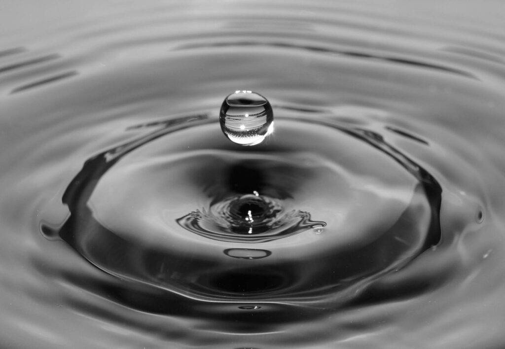 scatto in bianco e nero di una goccia d'acqua che cade formando un cerchio di onde - tu sei il centro