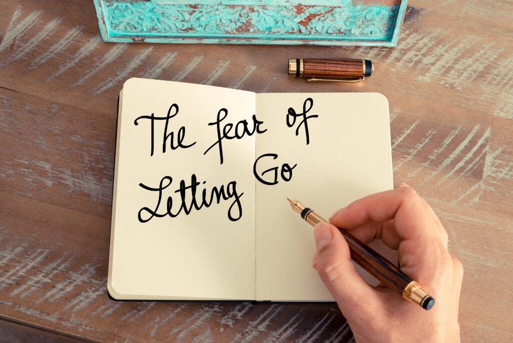 Handwritten text The Fear Of Letting Go as concept image. Retro effect and toned image of a woman hand writing a note with fountain pen on a notebook while writing about emotional growth