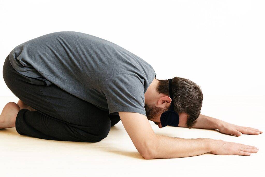 blindfolded boy bent over on the ground wearing a black mask practising Osho Mahamudra meditation